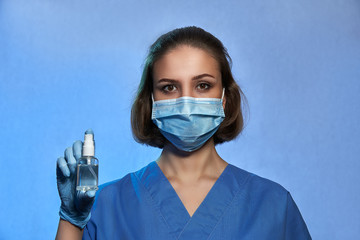 Medic, doctor, nurse in protective mask and in medical gloves with bottle of an antiseptic, isolated on studio background. Coronavirus COVID-19 disinfection, pandemic