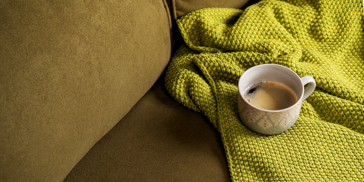 Fabric velvet green sofa with green soft knitted blanket plaid and big mug with coffee. Copy space for text, mockup with copy space. Stay ay home. cozy home.