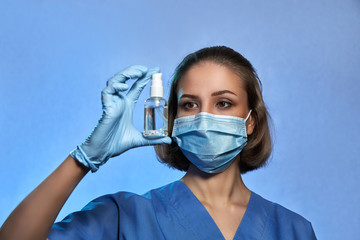 Medic, doctor, nurse in protective mask and in medical gloves with bottle of an antiseptic, isolated on studio background. Coronavirus COVID-19 disinfection, pandemic