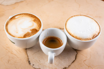 Three cups of decaffeinated coffee with milk, coffee with milk and black coffee. Light marble...