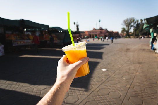 Hand holding a cup of fresh orange juice in Jemaa el-Fnaa square in Marrakesh, Morocco