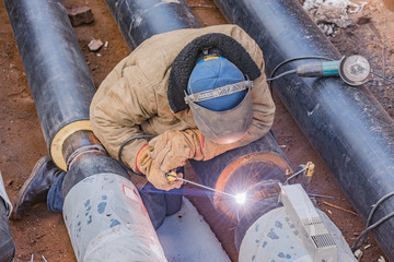Welder worker welds new metal pipe on the construction site.