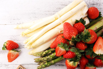 White and green asparagus with strawberries on rustic background with Spargelzeit wooden letter.