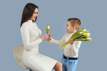 Happy mother's day6 The son the child congratulates mother and gives her flowers of tulips. Mom and son are smiling and hugging. Family holidays and communication. - Powered by Adobe