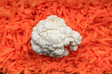 Big white Cauliflower in the middle of horizontal picture with orange background of grated fresh carrot. Vegetable pattern of vegan raw food lunch.