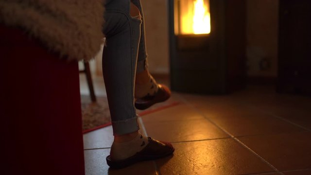 Close-up of shaking girl's leg on background of burning fire in pellet stove. Relaxation at home in cold winter weather, getting warm after coming back home from outside. Biofuel concept