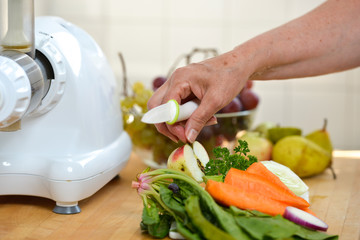 Woman putting vegetables and fruits in extractor to make delicious colored juice