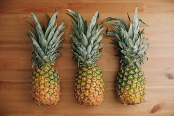 Three pineapples stand on a wooden table. Pineapples and cactus fruits are on the table. Exotic fruits.