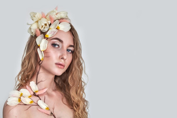 Obraz na płótnie Canvas Beautyful girl with tulip flowers in her hair, petals and color painting on her body. Cosmetic, beauty and make-up. Spring or summer concept. Photo on a grey background with place for your text.