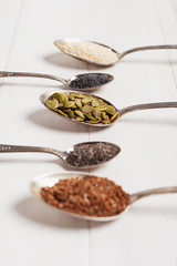 Superfoods in metal spoons on a white wooden background. Top view