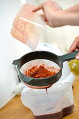 woman filtering fruit and vegetable juice with a sieve