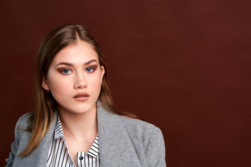 Independent young woman posing in the photostudio. Gorgeous young female in classic suit and grey coat.