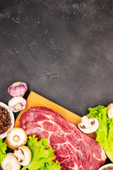Raw fresh marble meat steak and seasonings on a dark marble background, top view. fresh greens with mushrooms, garlic and beef
