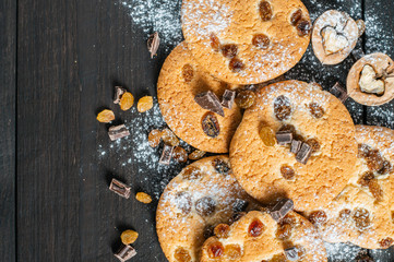 Naklejka premium Oatmeal cookies with raisins, chocolate and nuts sprinkled with powdered sugar lie on a dark wooden background