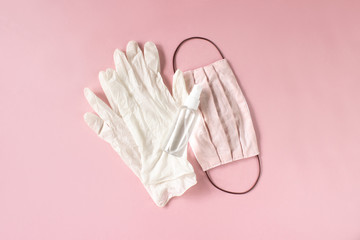 Sanitizer spray bottle, pair of rubber gloves and handmade mask flat lay on pink background top view. Means of protection. Coronavirus prevention, disinfecting, personal hygiene. Stock photo.