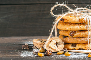 Oatmeal cookies with raisins, chocolate and nuts sprinkled with powdered sugar tied with linen thread on a brown wooden background