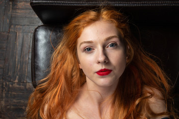 From above close up beauty portrait of young adorable red-haired woman with bare shoulders in studio lying on black sofa