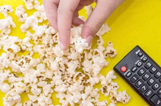 Popcorn And Remote Control, Top View On A Yellow Background. People Eat Popcorn. Human Hands. View From Above.