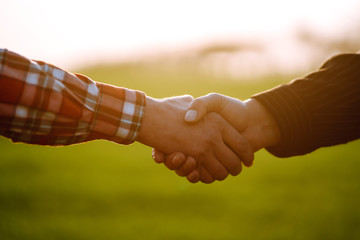 Handshake two farmer on the background of a wheat field at sunset. The concept of the agricultural...