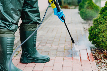 Man cleaning red, conrete pavement block using high pressure water cleaner. Paving cleaning...