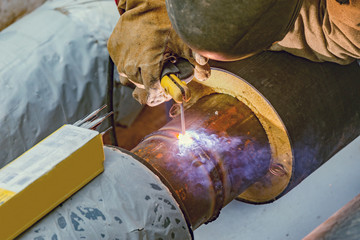 Welder worker welds new metal pipe on the construction site.