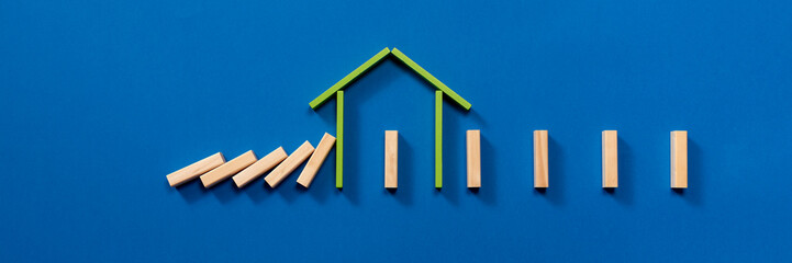 A wooden house stops the collapse of the pieces of domino wood. Visual scheme that explains the importance of maintaining social distance and isolation between people to avoid virus infection.