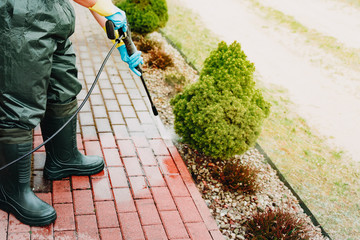 Man cleaning red concrete pavement block using high pressure water cleaner. Paving cleaning...