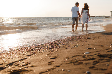 Happy lovers walk along the seashore in the lohs of the setting evening sun