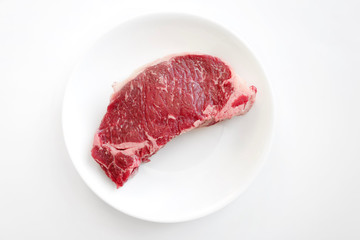 Fresh raw beef steak in white plate isolated on white background. Meat prices rise and global food crisis due to Coronvavirus global covid-19 pandemic. Selective focus, top view and close up.