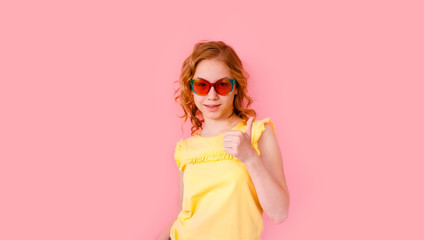 Emotional blonde teen girl in sparkle sunglasses and yellow t-shirt laughing to camera on pink background, space for text.