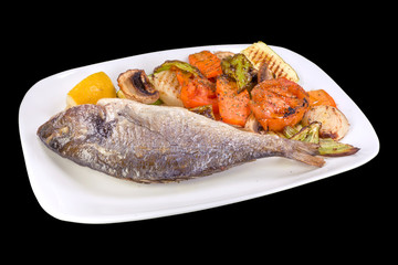 Grilled sea bream or Dorada with steamed vegetables and mushrooms on a white plate, isolated on black background