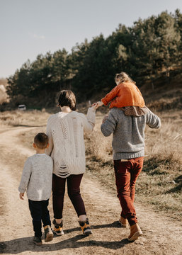 Family of four walking on a dirt path in a forest, wearing sweaters on warm autumn sunny day.