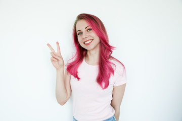 Pretty young girl with pink dyed hair smiling while showing two fingers peace sign. Beautiful smile. 
