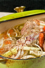 Top view, close distance of a green, cast-iron pot, with  lid filled with chicken, sliced carrots, sweet onion, celery, and Italian spices, to be roasted for homemade chicken soup