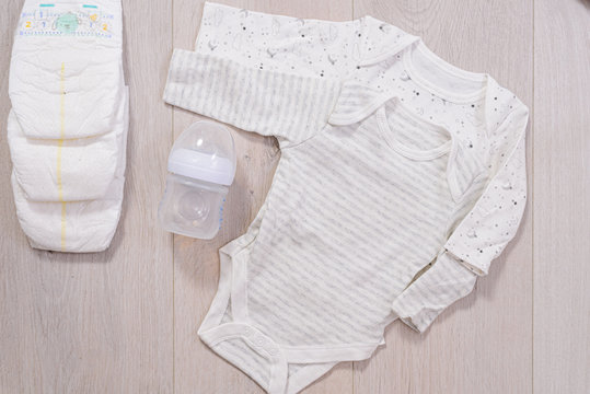 white baby clothes, diapers and baby milk bottle wooden background. newborn