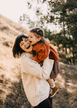 Mother and daughter playing outside on a sunny day. Mother hugging child, having fun together.