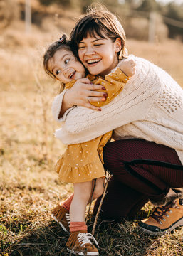 Mother and daughter playing outside on a sunny day. Mother hugging child, having fun together.