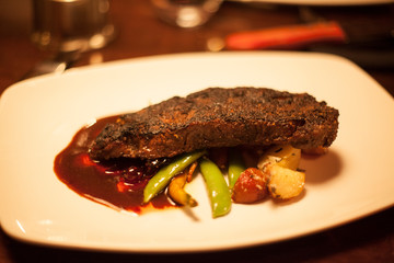 Steak and vegetables in a red sauce on a white plate.
