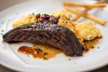 A main course at a restaurant in the French Riviera. with Veal steak with cranberry sauce and polenta