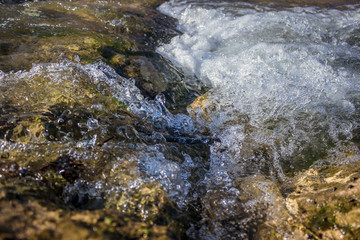 Fast flowing natural stream, close up. Clear fresh water splattering, drops and foam of the mountain creek. Water conservation concept.