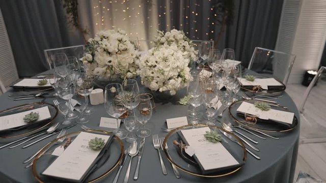 Tender bouquets made of white eustomas and greenery on the served grey round table, film sliding from bouquet to the whole decorated room