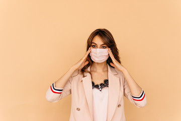 Office worker wearing facial mask, protecting her hands and face to prevent contagious disease, isolated on yellow background