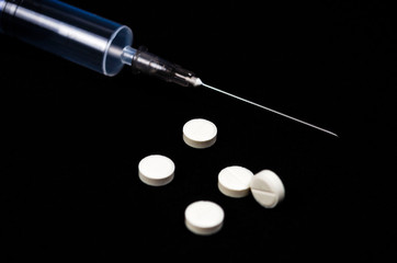 Medical preparations, pills and syringe lie on black background.