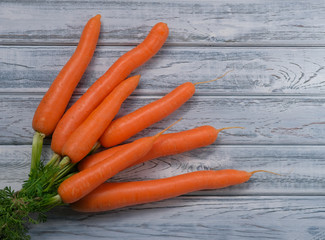 Bunch of fresh sweet carrot on light wooden background with copy space. Organic carrots with green leaves on old white wood table. Healthy food, harvest of vegetables.