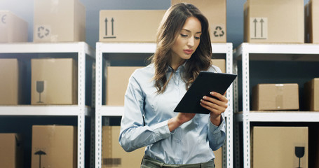 Beautiful woman, postal worker with tablet device in hands working in post office.