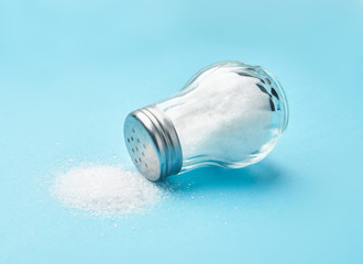 Salt shaker and fine salt isolated on blue background.