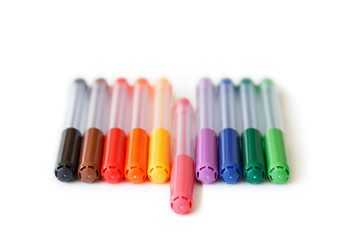 Close-up of set of colorful rainbow colored marker pens in a row, low angle view. Pink marker in the middle is apart. Concept of standing out. Isolated on white background.