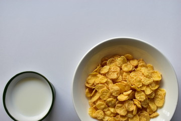 A Cup of yellow cornflakes in milk on a white background