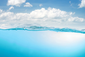 Blue water wave with splash and bubbles surface on blue sky with white clouds
