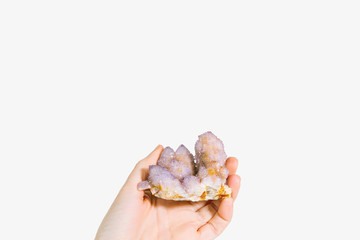 Young woman's hand holding a purple amethyst quartz crystal / isolated on gray background